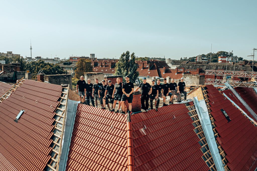 Team der Dachbau Stefan Höft GmbH auf einem Berliner Altbaudach mit Blick über die Stadt