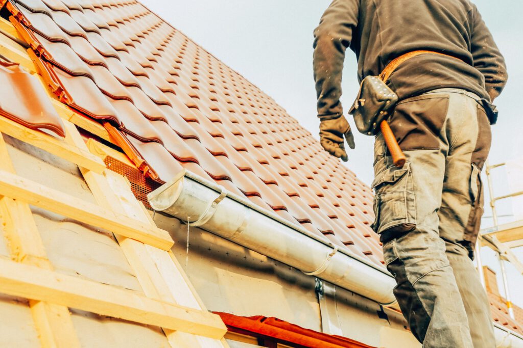 Dachdecker kontrolliert Dachrinne und Eindeckung eines Steildachs